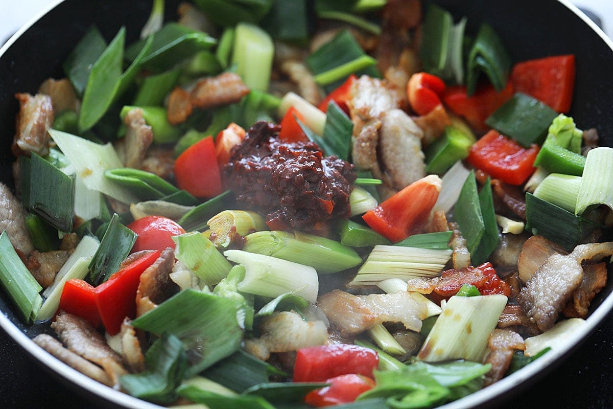 Pork belly, green and red bell peppers, and spicy doubanjiang in a wok.