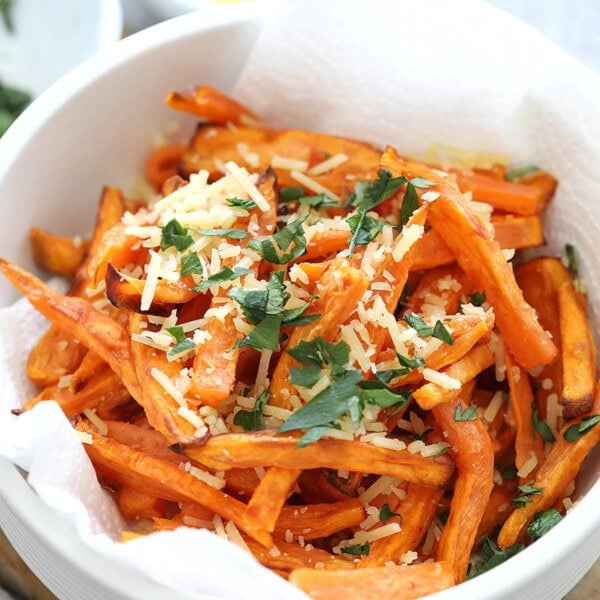 Air fried sweet potato fries in a bowl, topped with Parmesan cheese and parsley.