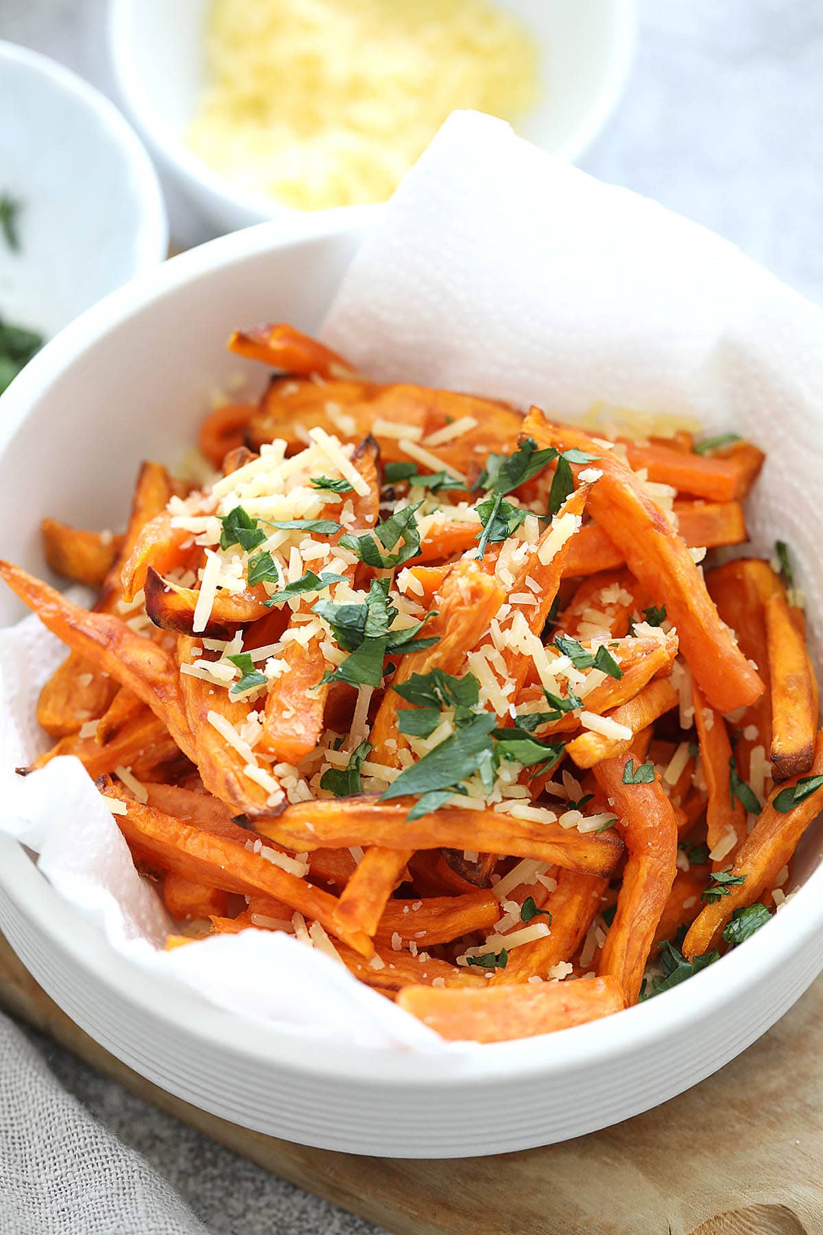 Air fried sweet potato fries in a bowl, topped with Parmesan cheese and parsley.