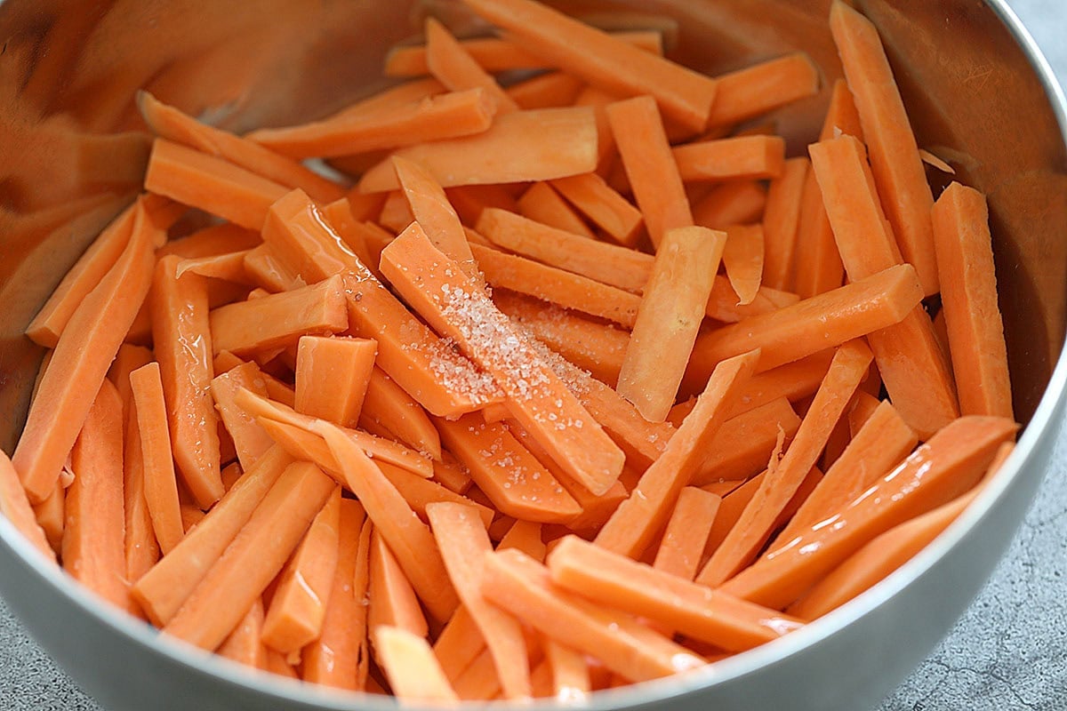 Sweet potato strips in a bowl with olive oil and salt.