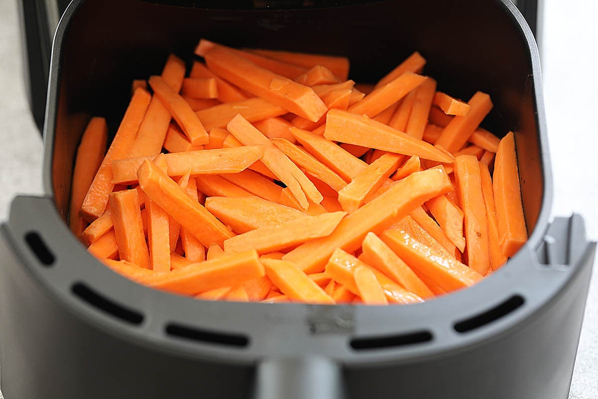 Seasoned sweet potato strips in the air fryer basket.