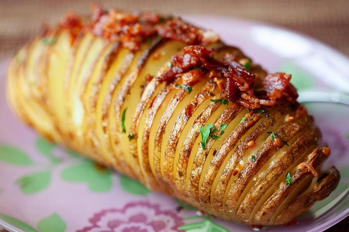 Baked Hasselback potatoes with cheese and crispy bacon on a plate.