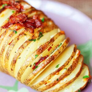 Cheesy Hasselback potato with crispy bacon, served on a plate.