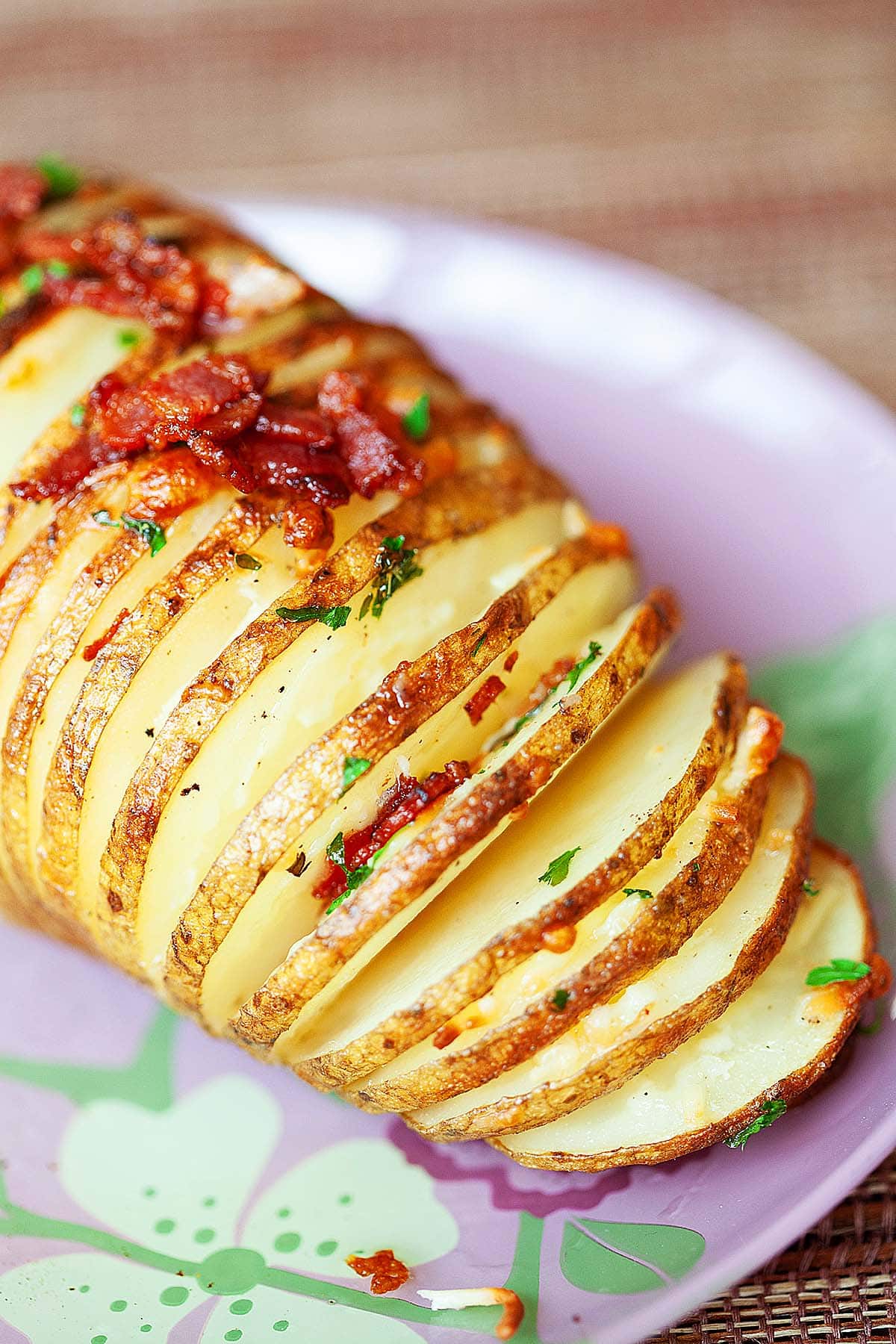 Cheesy Hasselback potato with crispy bacon, served on a plate.