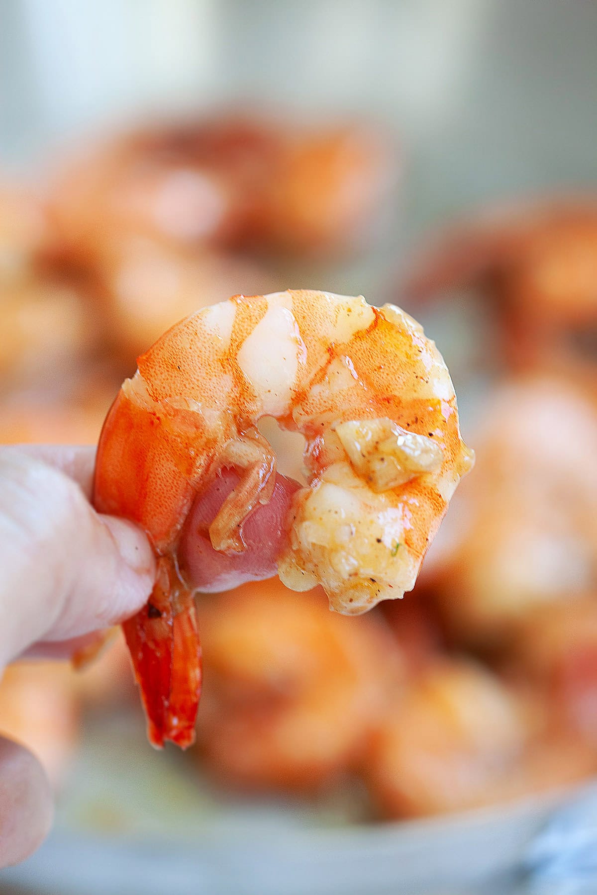 Peeled Hawaiian garlic shrimp held with fingers.