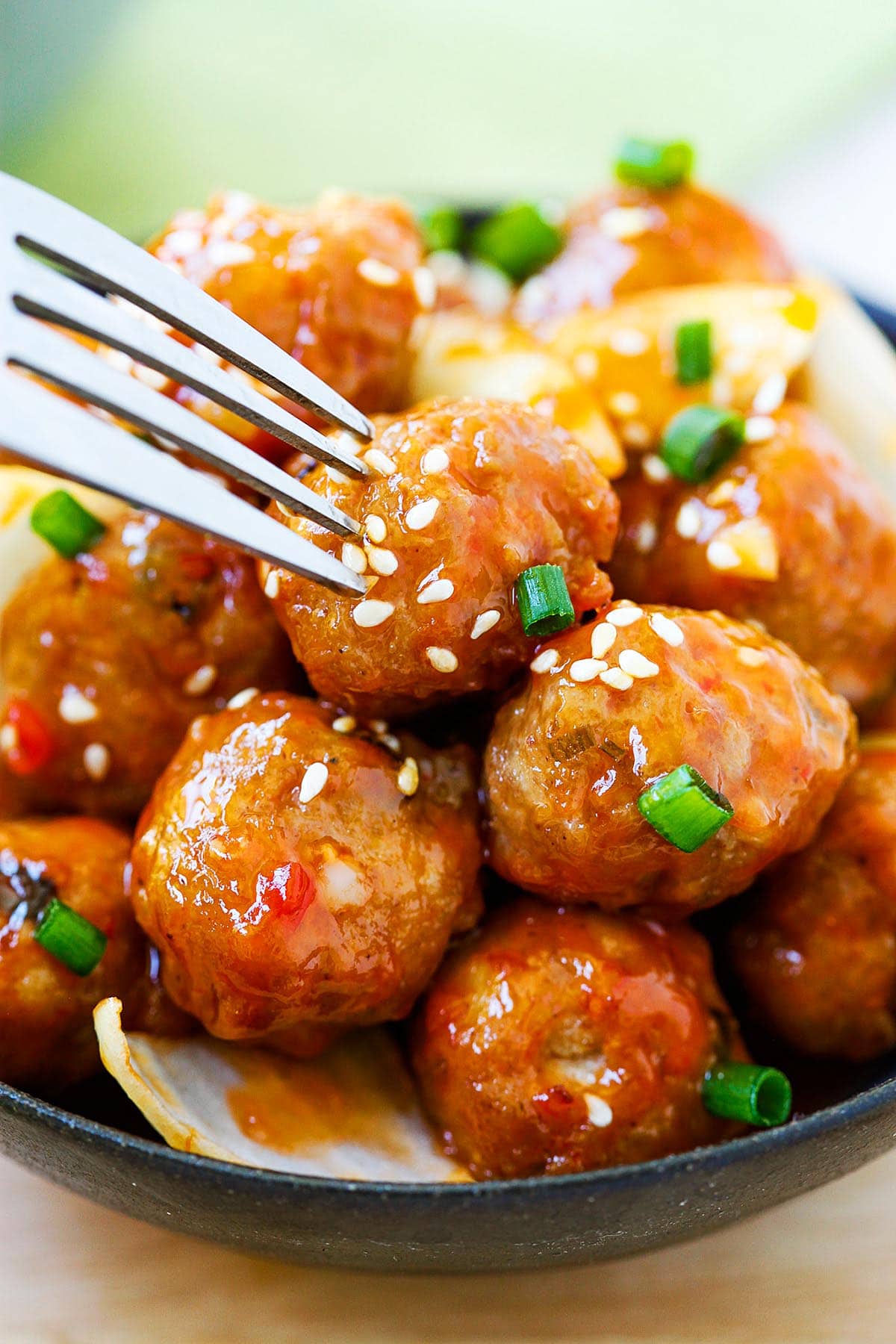 Sweet and sour meatballs coated in glossy sauce, with a fork poised to pick one up.