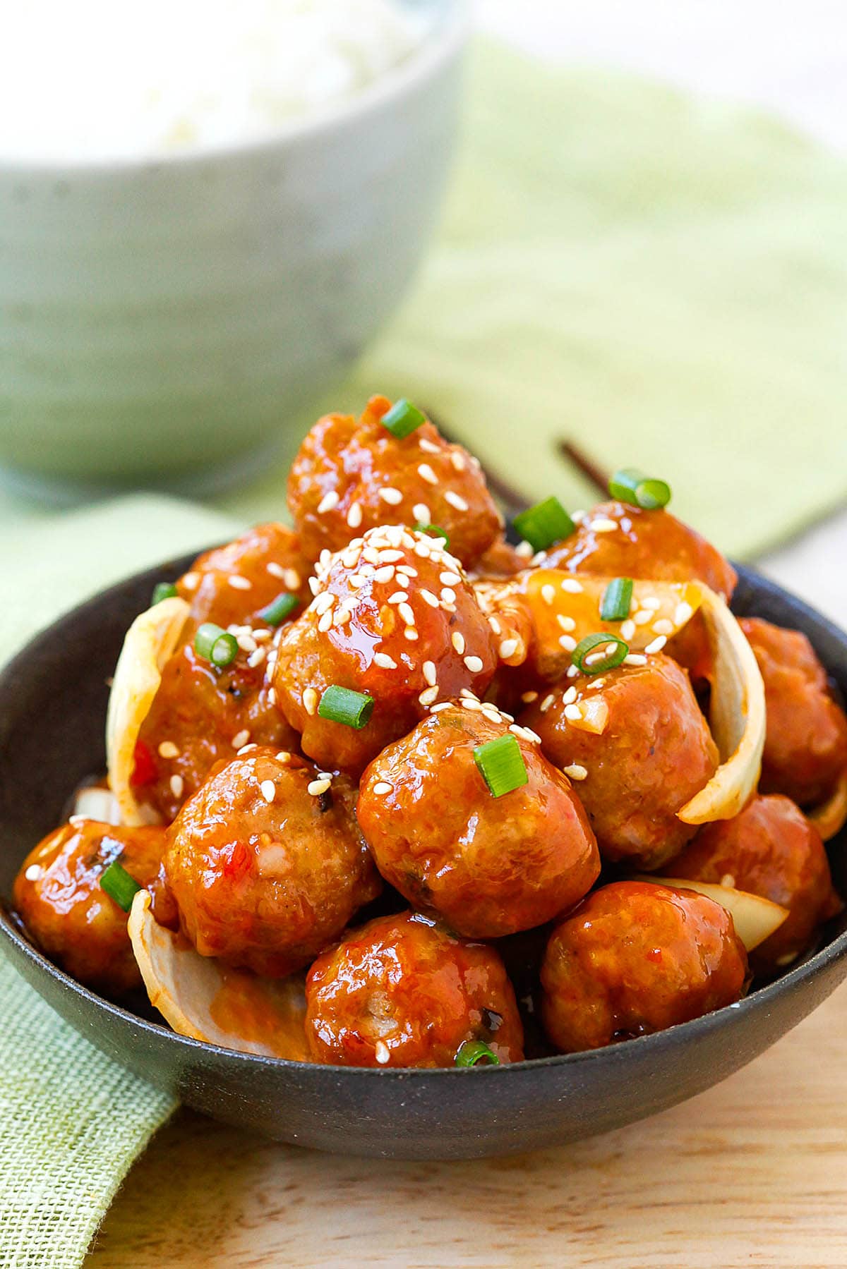 Sweet and sour meatballs garnished with green onions and white sesame seeds.