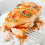 Flaky sweet chili salmon with a sticky glaze, topped with fresh cilantro, served over a bowl of white rice.