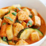 A bowl of chicken zucchini curry with carrots.