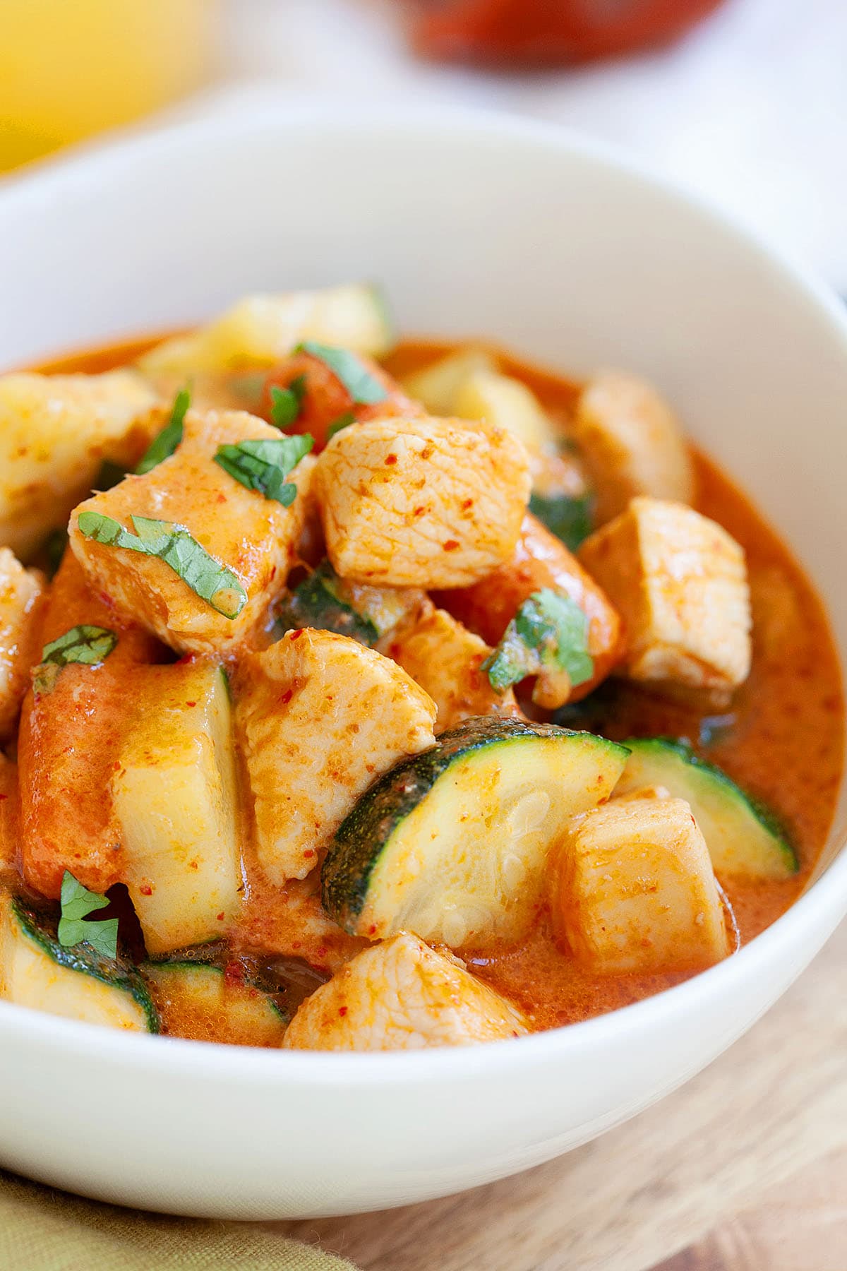 A bowl of chicken zucchini curry with carrots.