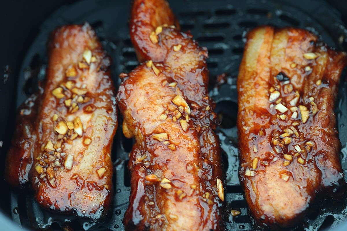 Marinated pork belly with remaining marinade spooned over it in the air fryer basket.