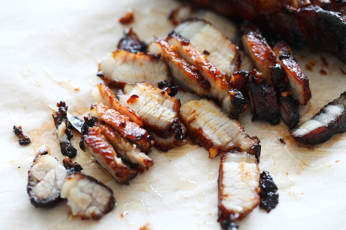 Sliced air fryer char siu on a chopping board lined with parchment paper.