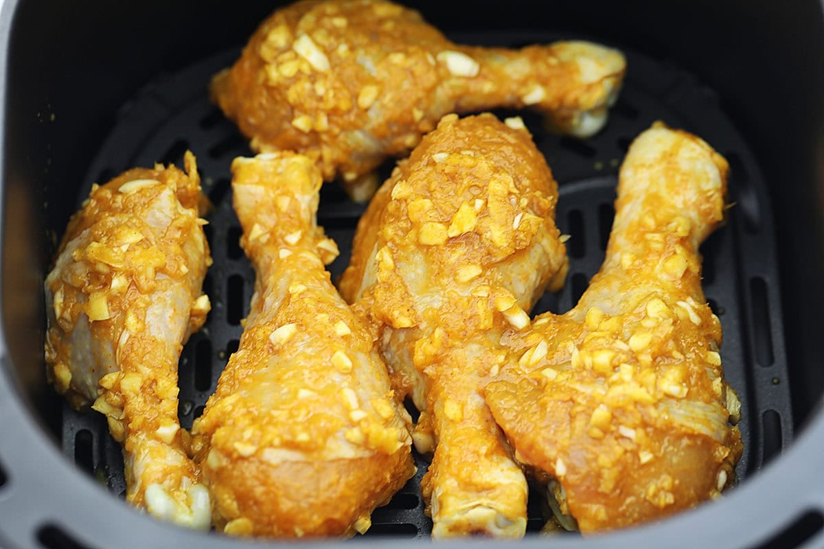 Marinated chicken legs arranged in a single layer in the air fryer basket.