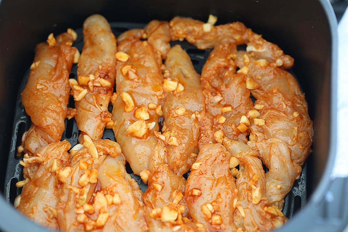 Chicken tenders placed in a single layer inside the air fryer basket.