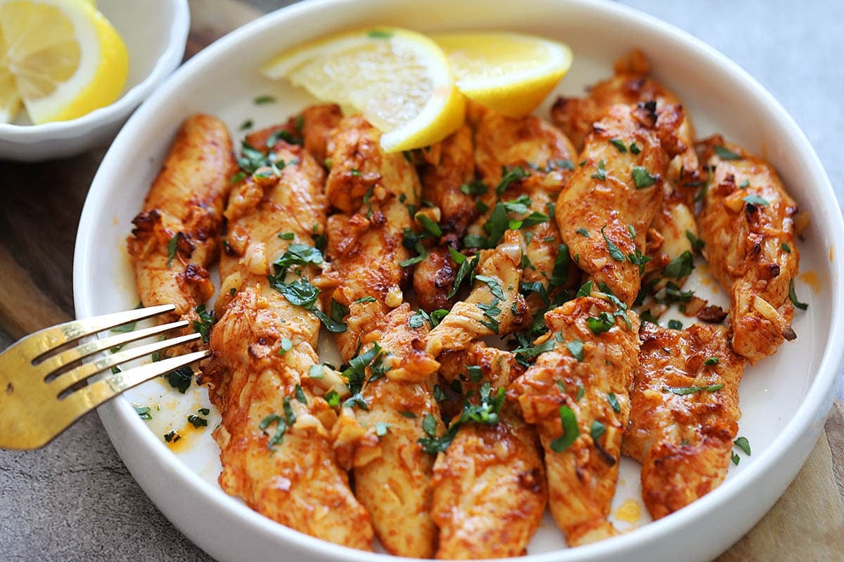 Juicy, golden chicken tenders fresh out of the air fryer, served with lemon wedges and parsley.