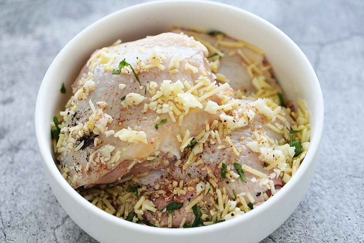 Chicken thighs coated in garlic parmesan seasoning in a bowl.