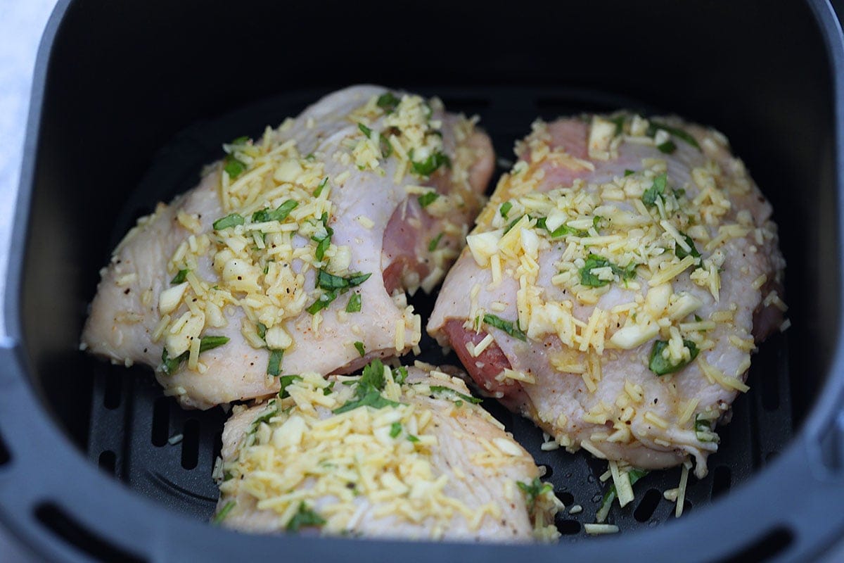 Chicken thighs seasoned with garlic parmesan in the air fryer basket.