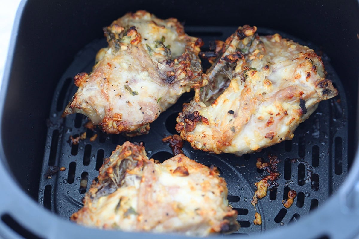 Golden brown garlic parmesan chicken thighs in the air fryer basket.