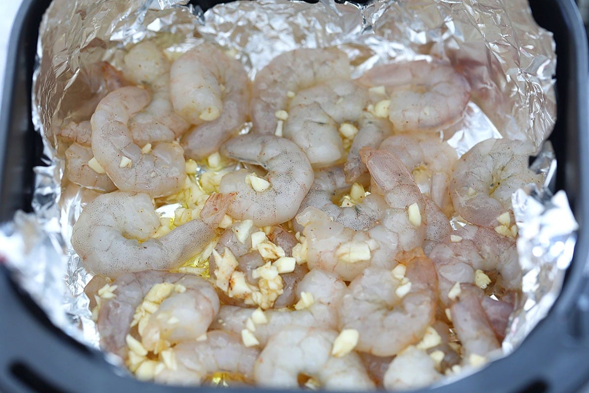 Shrimp coated in honey garlic sauce in an air fryer basket lined with foil.