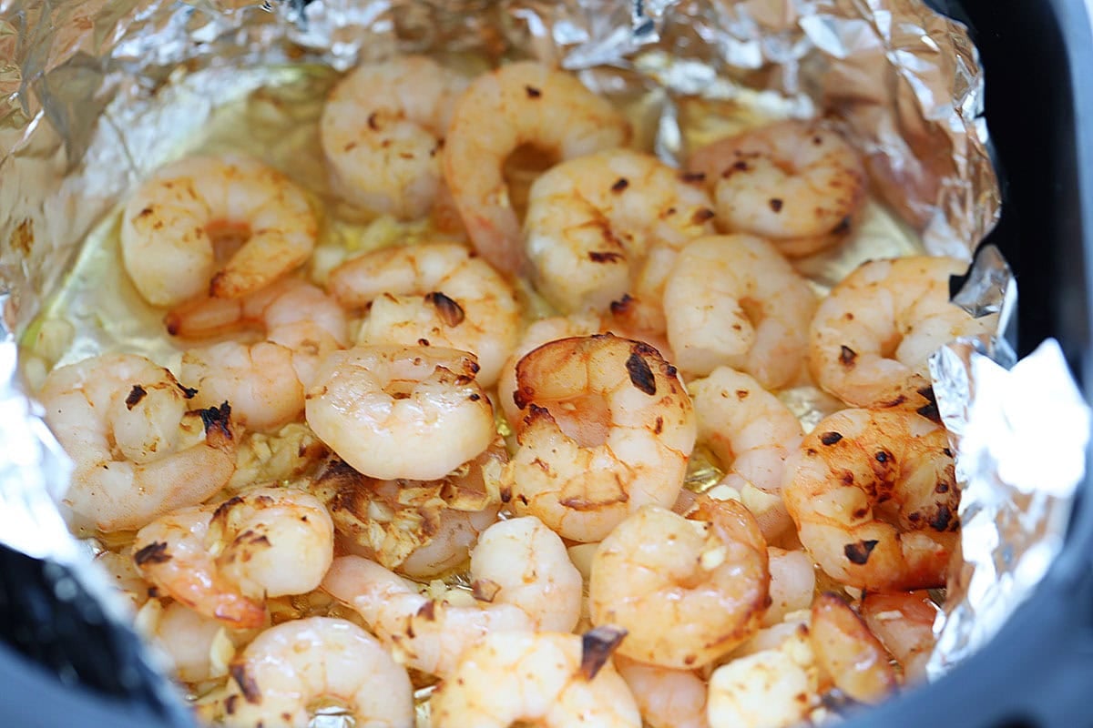 Cooked shrimp in an air fryer basket, coated in honey garlic sauce.