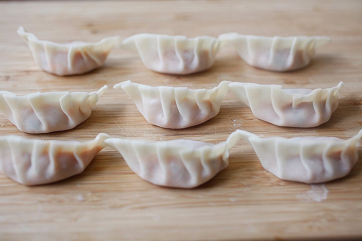 Uncooked kimchi dumplings lined up on a chopping board, prepped for pan-frying.