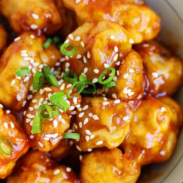 Crispy orange beef glazed in a sticky, glossy orange sauce, garnished with sesame seeds and green onions, served in a bowl.