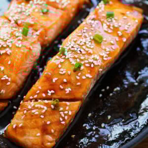 Honey teriyaki salmon garnished with white sesame seeds and spring onions.