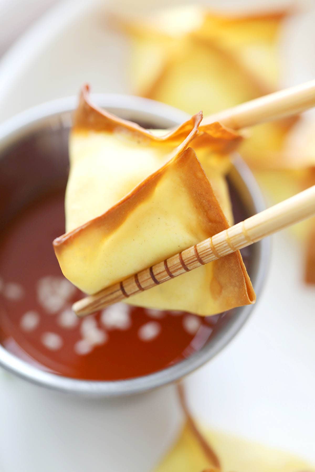 Crispy air fryer wontons with creamy filling, picked up with chopsticks and dipped in sweet and sour sauce.
