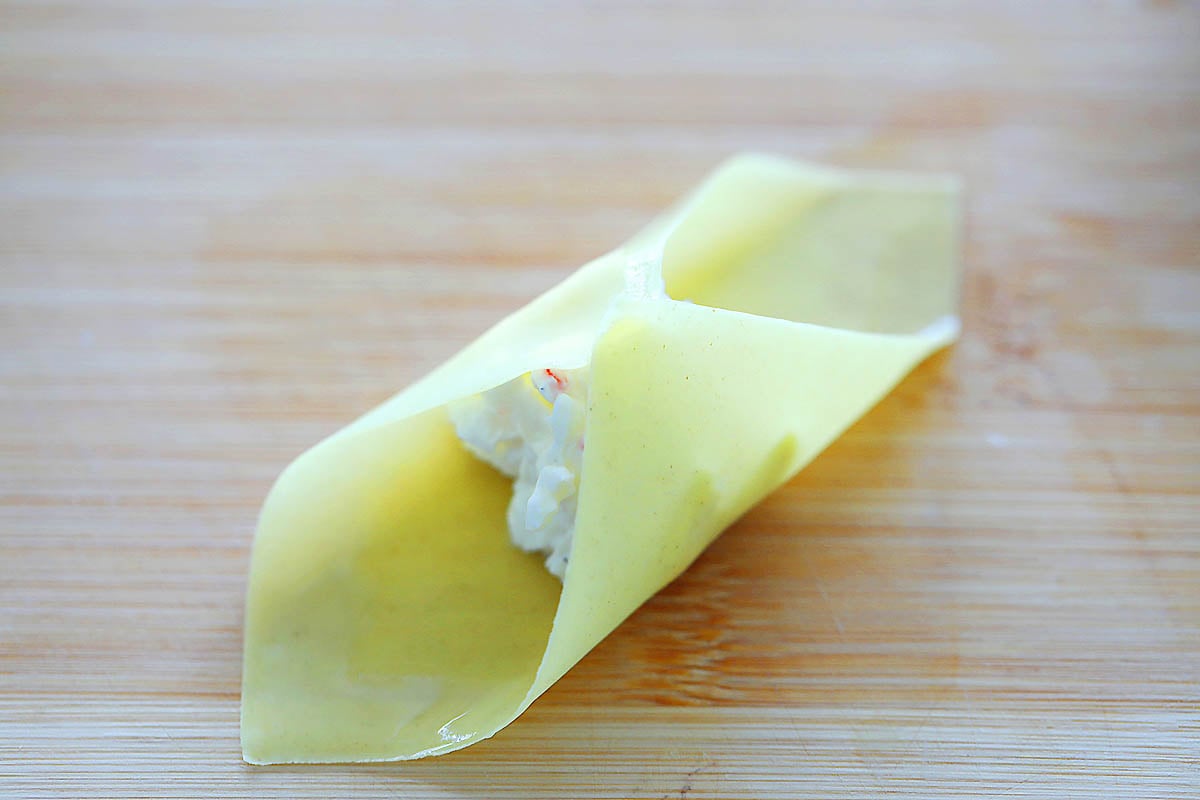 Wonton wrapper with filling in the center being folded.