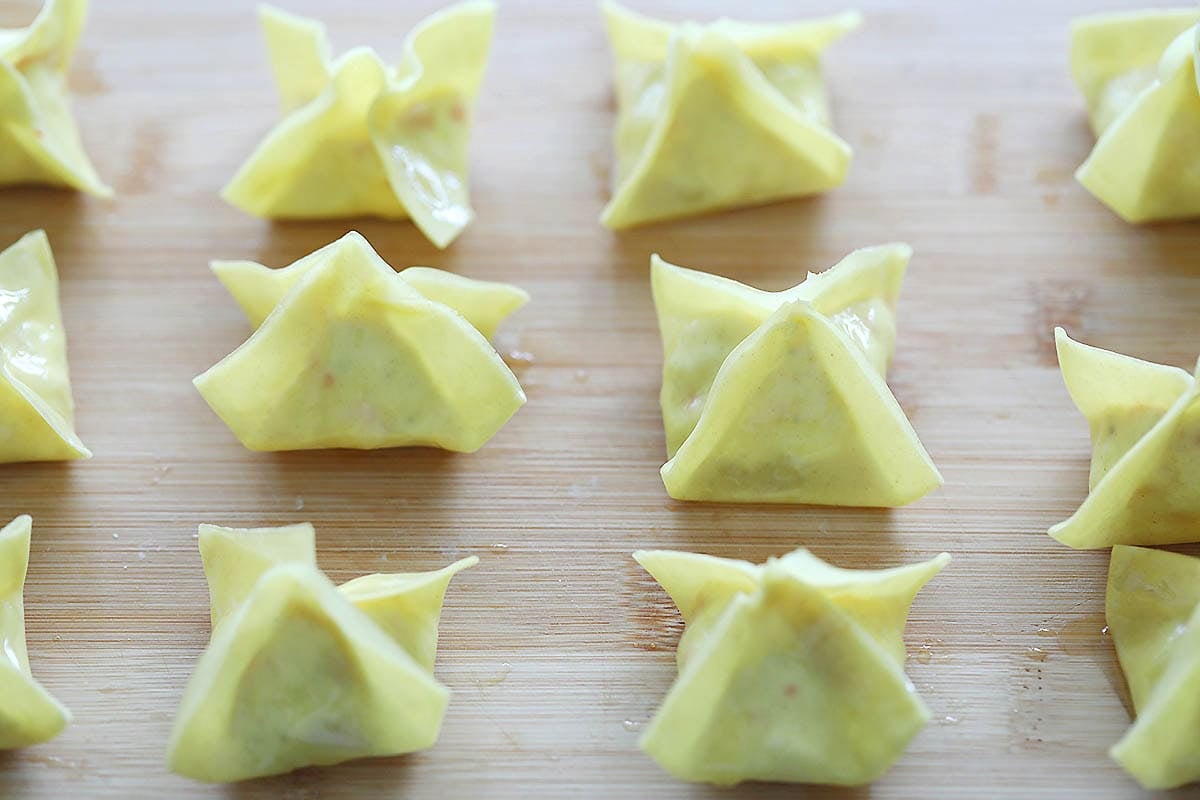 Sealed wontons on a chopping board.