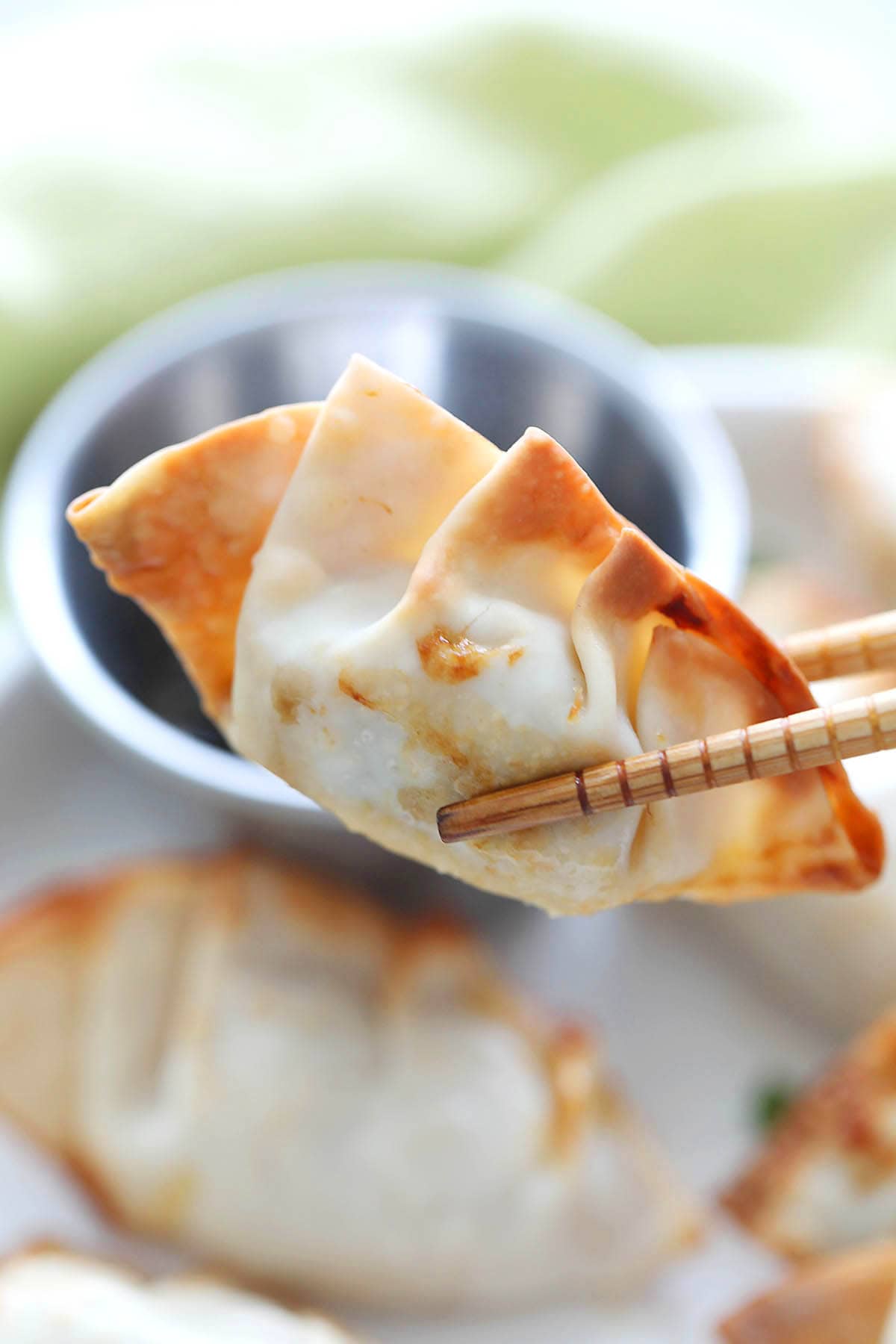 Crispy air fryer dumpling held with chopsticks over serving plate.