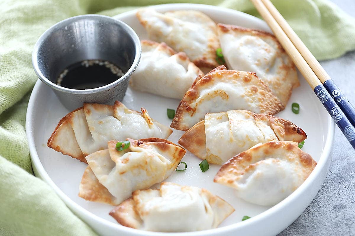 Air fryer gyoza served with ponzu sauce and scallion garnish on a plate.