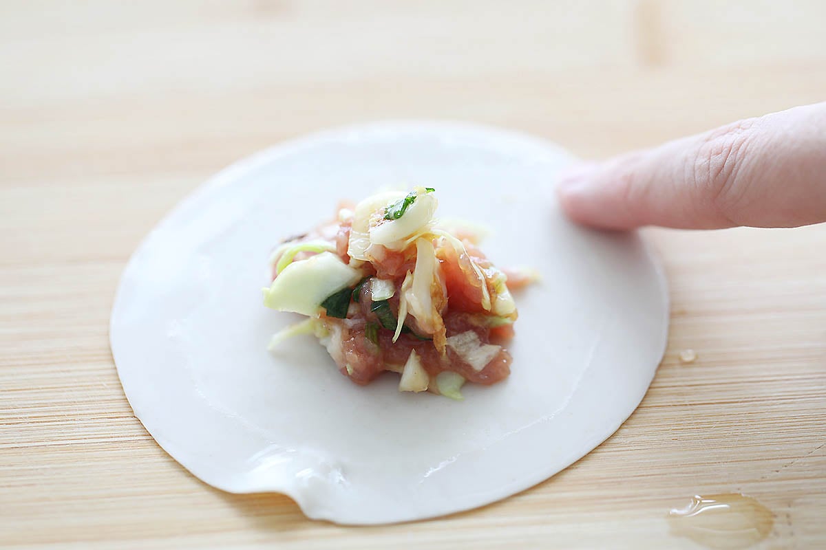 Gyoza filling placed in the center of a wrapper with finger wetting the edges.