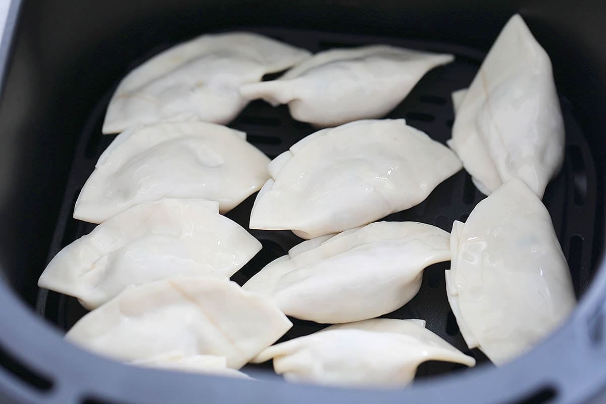 Uncooked gyoza in an air fryer basket, flat side facing up.
