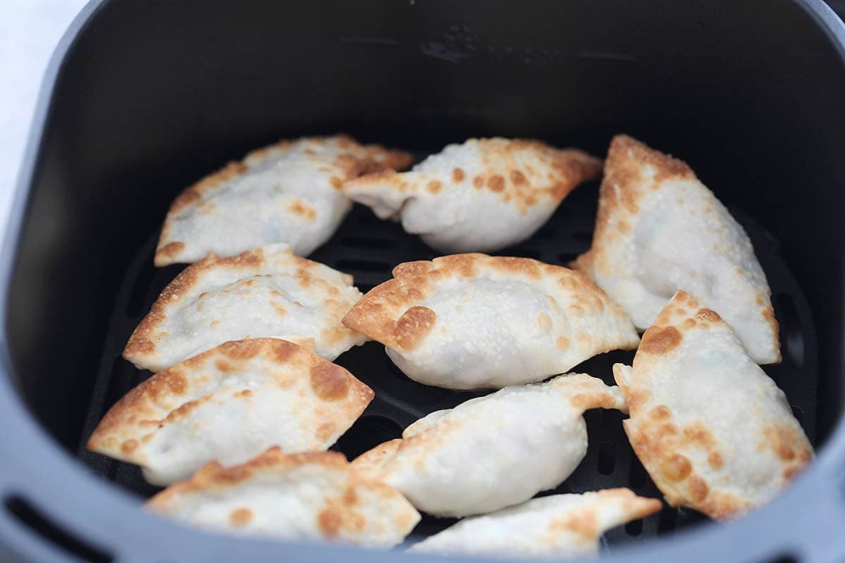 Golden crispy gyoza in an air fryer basket.