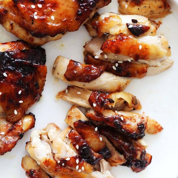 Air fryer honey chicken thighs topped with white sesame seeds, served on a plate.
