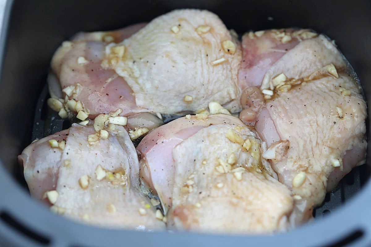 Marinated chicken thighs arranged in a single layer in the air fryer basket.