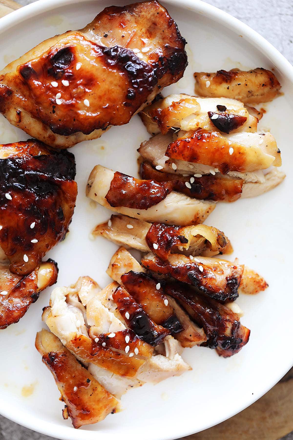 Air fryer honey chicken thighs topped with white sesame seeds, served on a plate.
