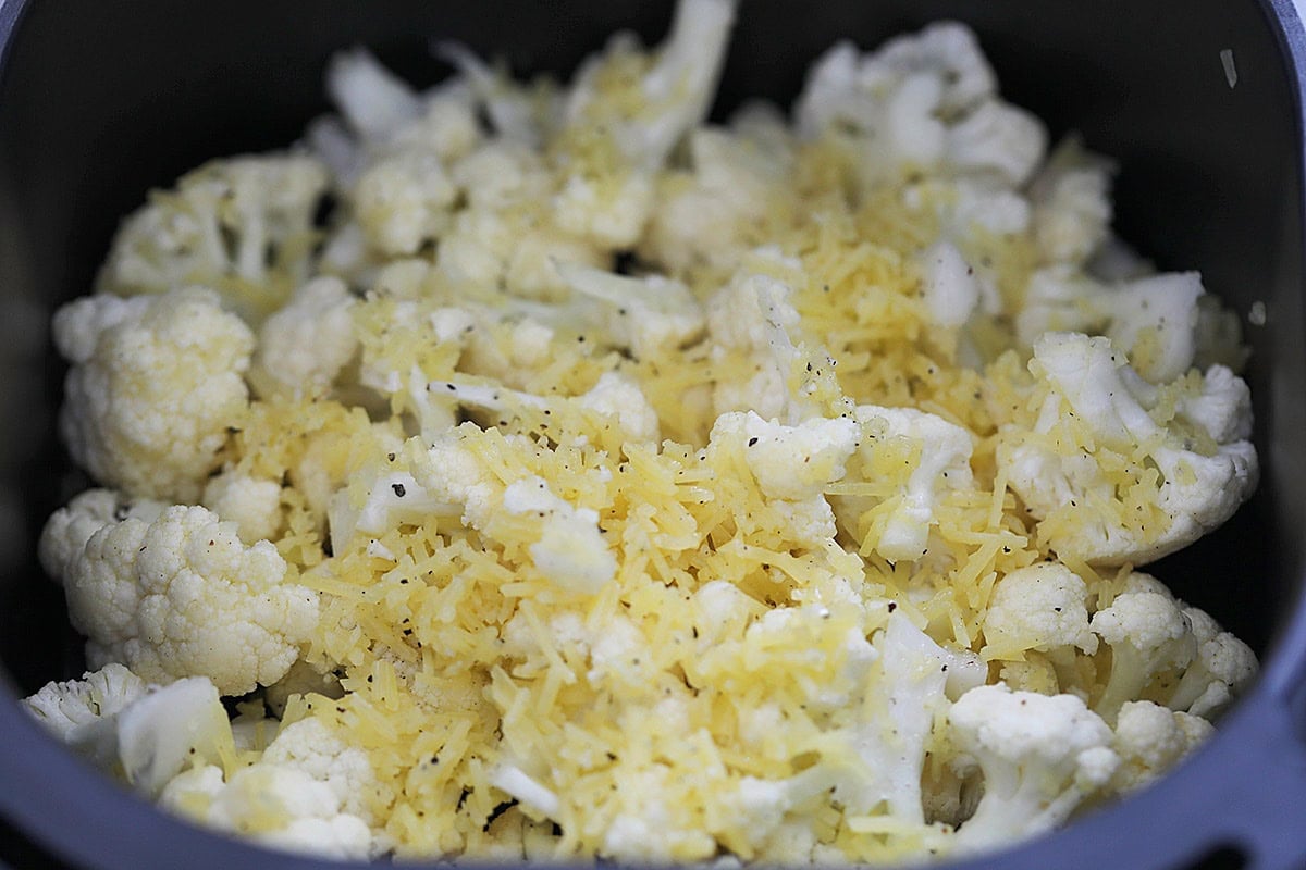 Seasoned cauliflower florets and Parmesan cheese in an air fryer basket.