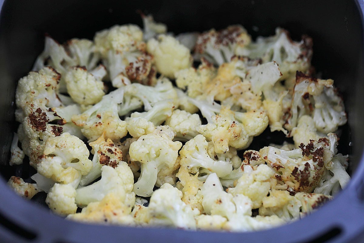 Parmesan cheese-coated roasted cauliflower in an air fryer basket.