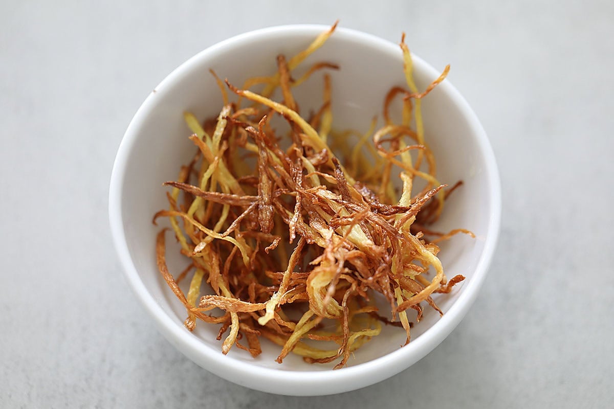 Golden brown fried ginger strips in a small bowl.