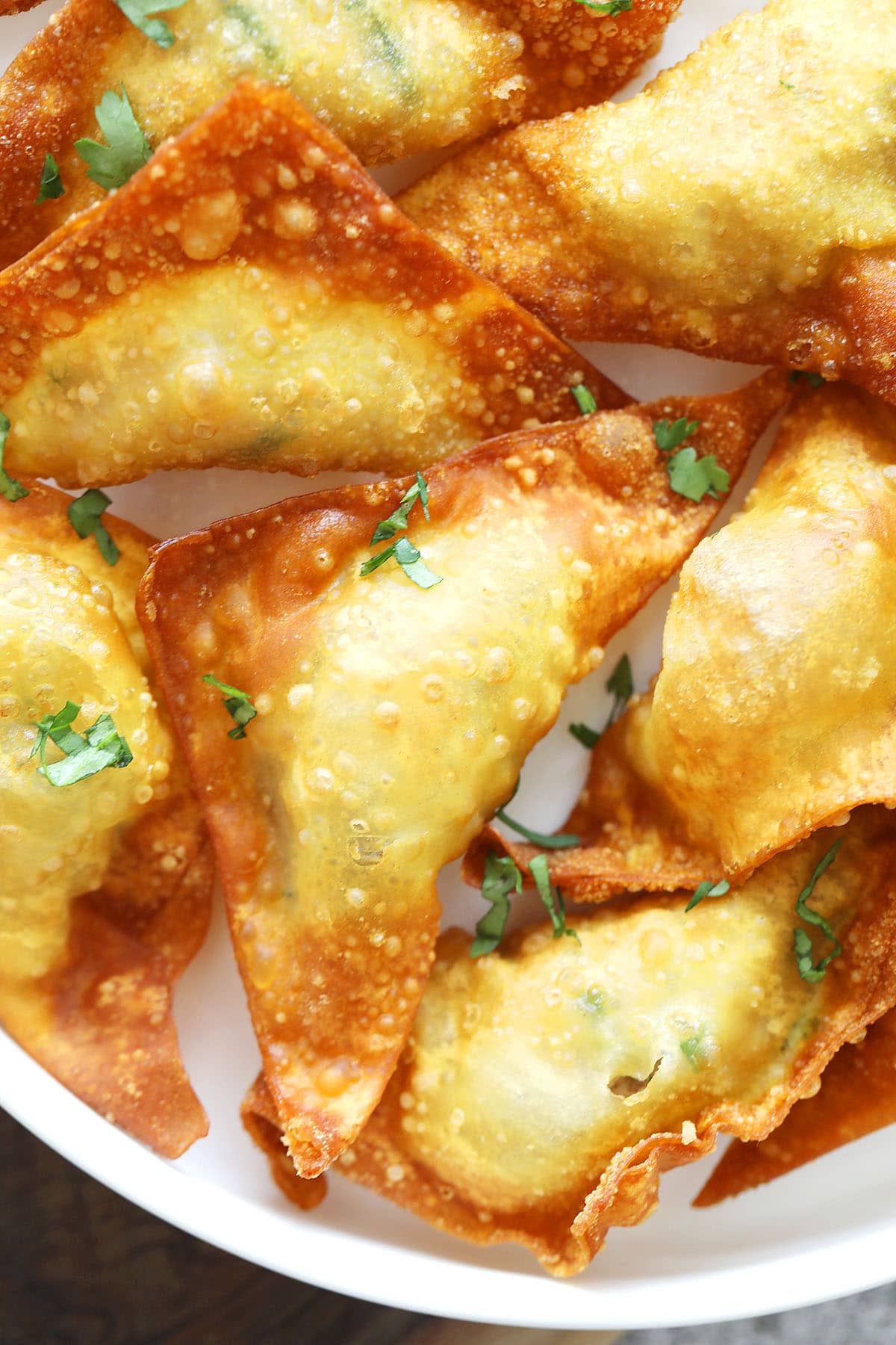 Triangle-shaped Thai fried wontons freshly deep fried on a white plate.