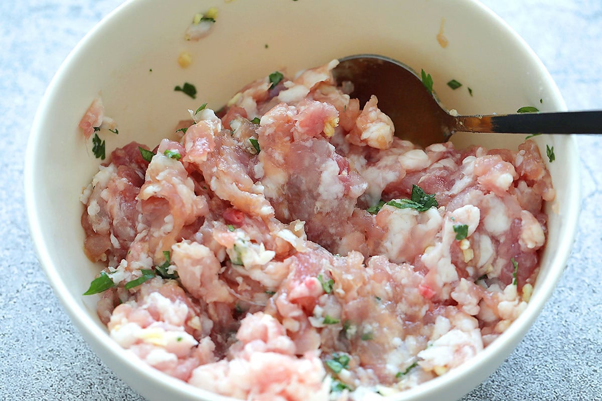 Ground pork with cilantro and seasoning in a bowl.