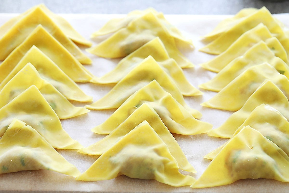 Triangle-shaped wontons with pork filling on a parchment paper.