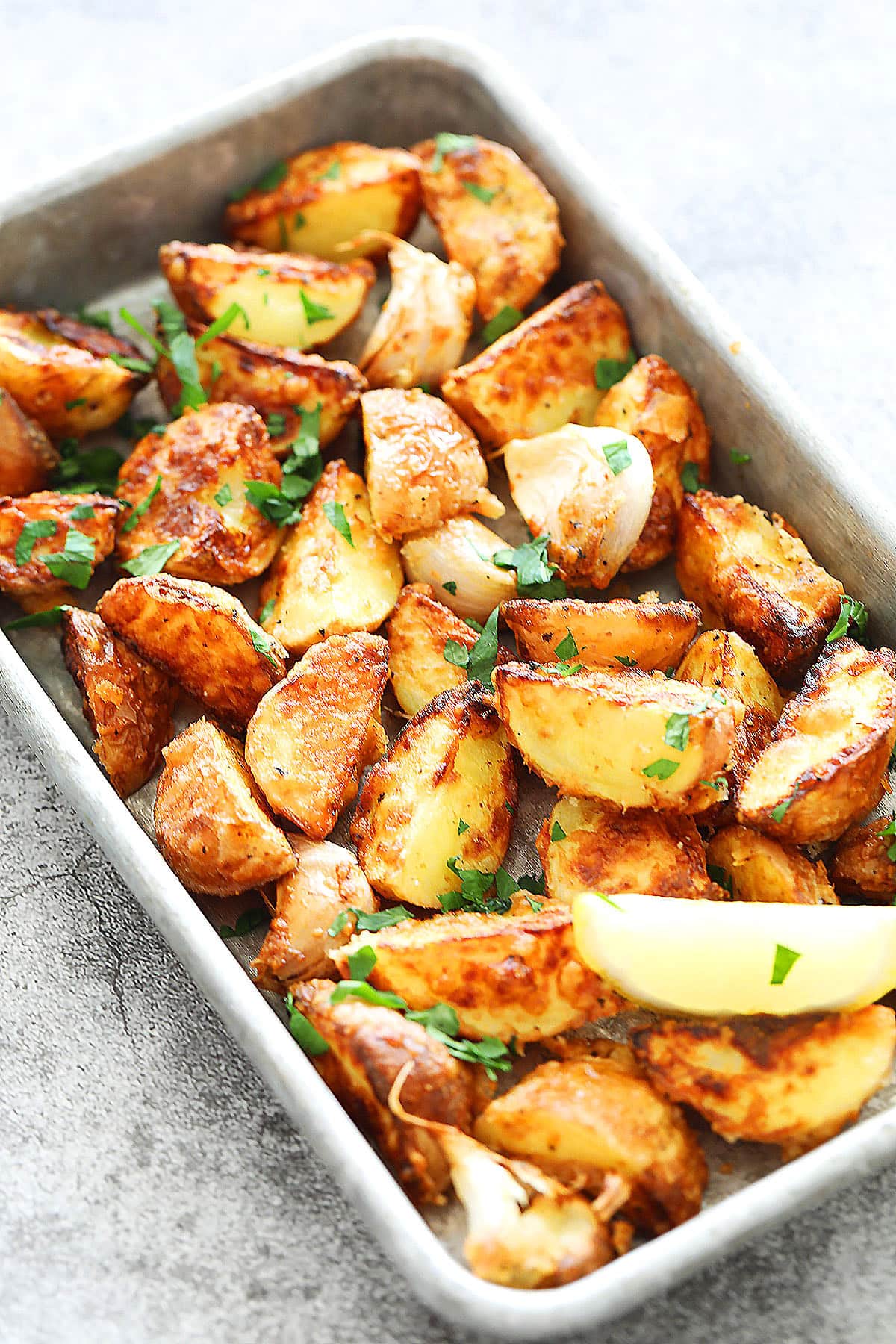Crispy air fryer baby potatoes in a rustic metal tray, garnished with fresh parsley and lemon wedges for serving.