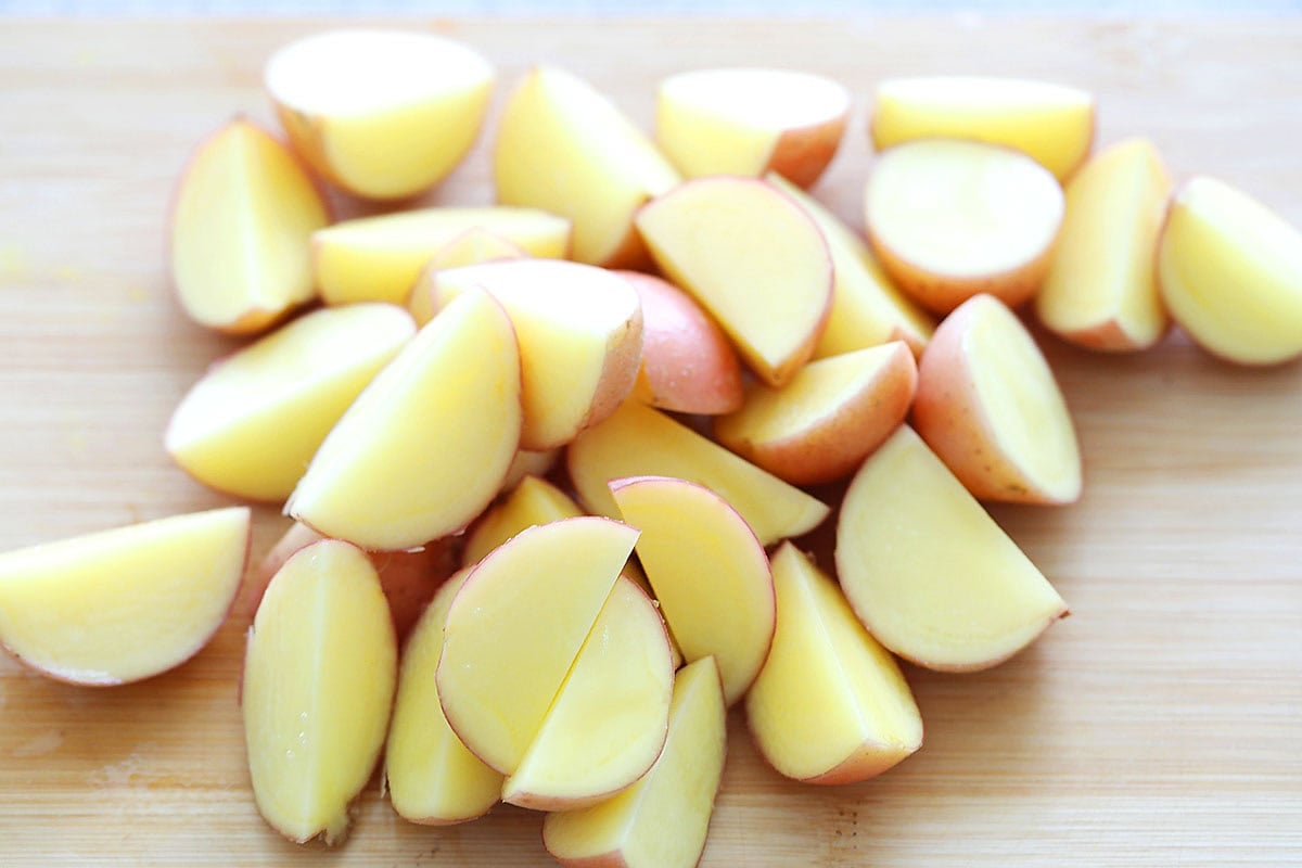 Raw baby red potatoes halved and quartered on wooden chopping board.
