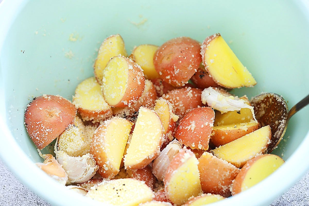 Halved baby potatoes tossed with garlic, olive oil, and Parmesan in a mixing bowl.