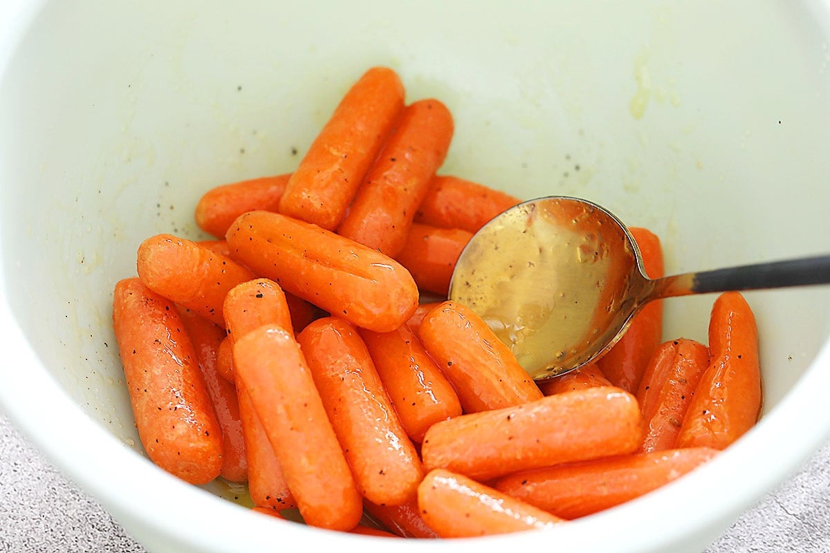 Baby carrots tossed with melted butter and honey in a bowl.