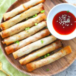 Crispy air fryer lumpia on a white plate next to a bowl of red chili sauce.