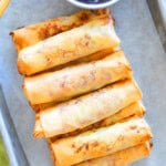 Golden crispy air fryer spring rolls with chili sauce on a tray.